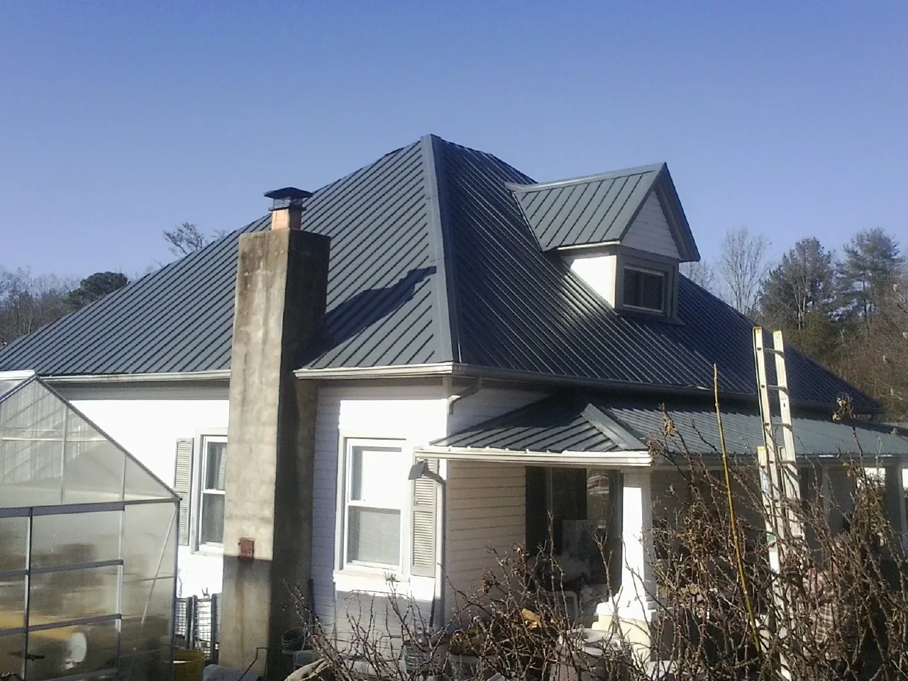 Dark blue standing seam metal roof on a white farmhouse with dormer — Slate & Tile Roof Repair by Roofing Brothers in Fort Gratiot