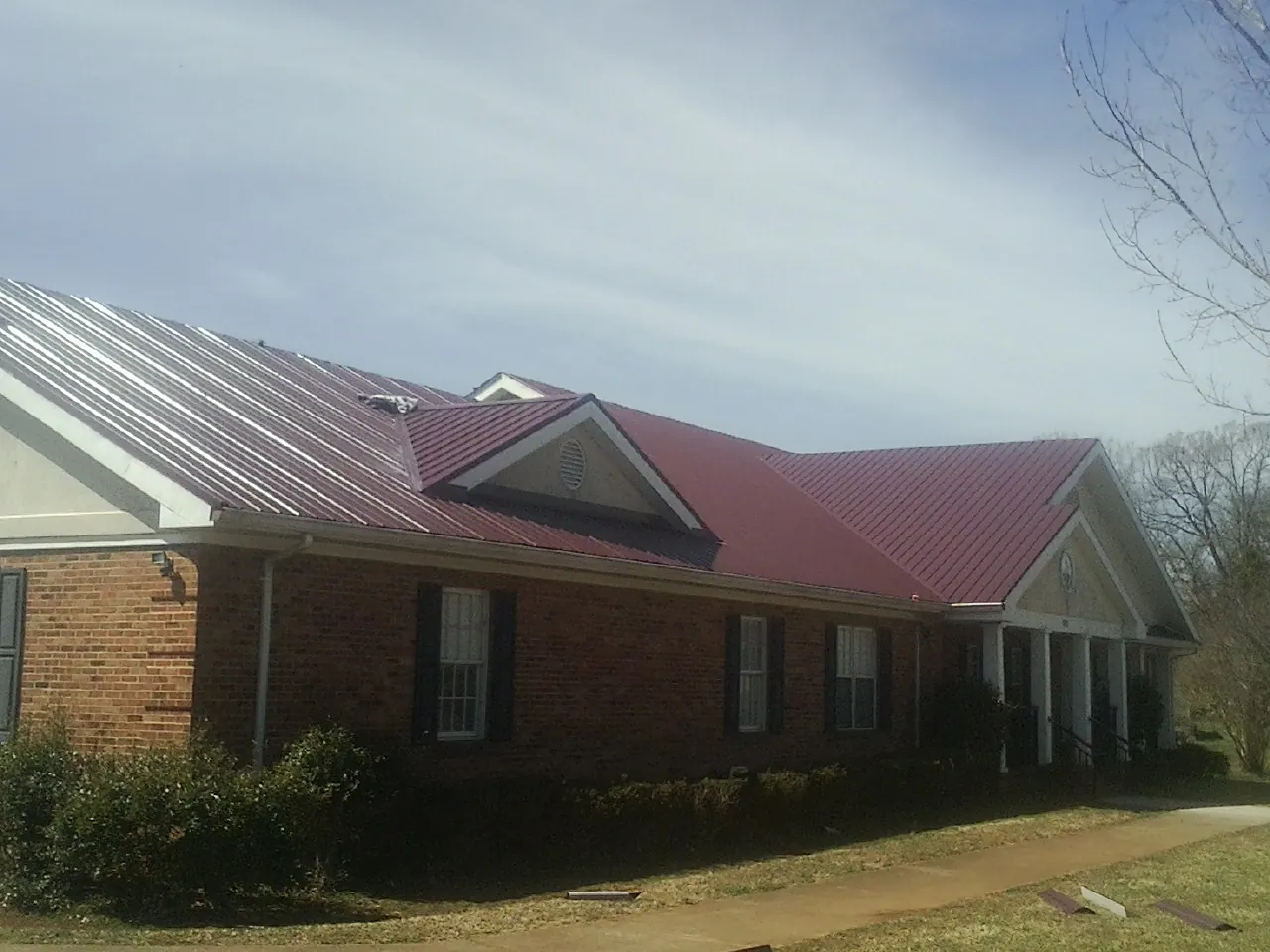 Red metal roof with gabled entries on a long brick building, from a Hail Damage Roof Repair job in Fort Gratiot