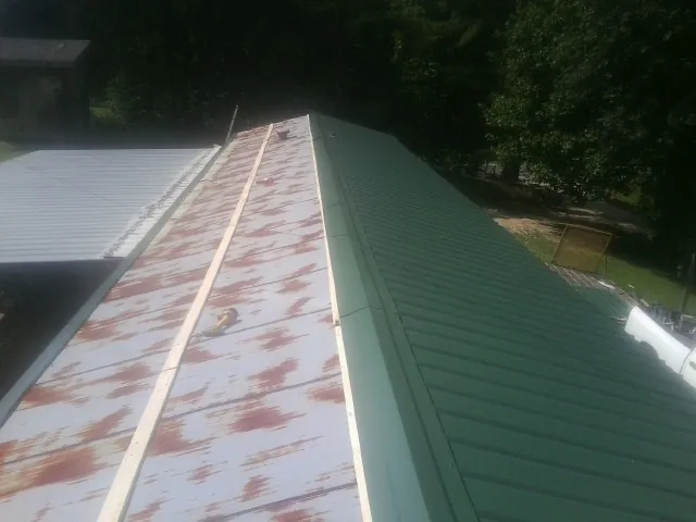 Old rusted panels beside newly installed green metal roofing — Wind Damage Roof Repair by Roofing Brothers in Fort Gratiot