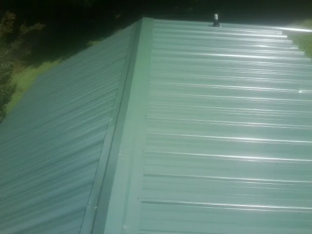 New green metal panels meeting at the ridge of a roof — Flat Roof Repair work by our crew in Fort Gratiot