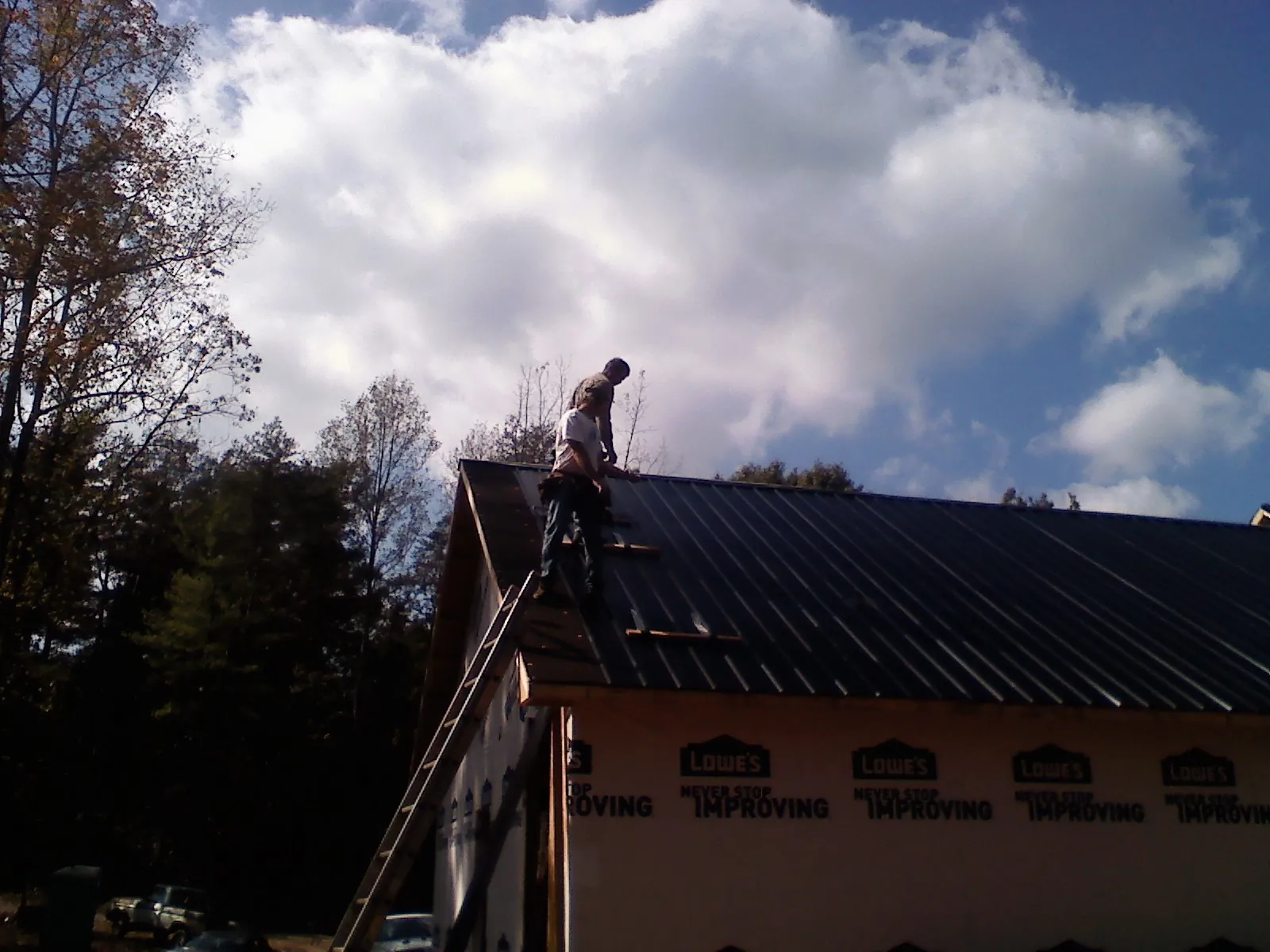 Roofer fastening dark metal panels high against a cloudy sky, from a Roof Inspection job in Fort Gratiot