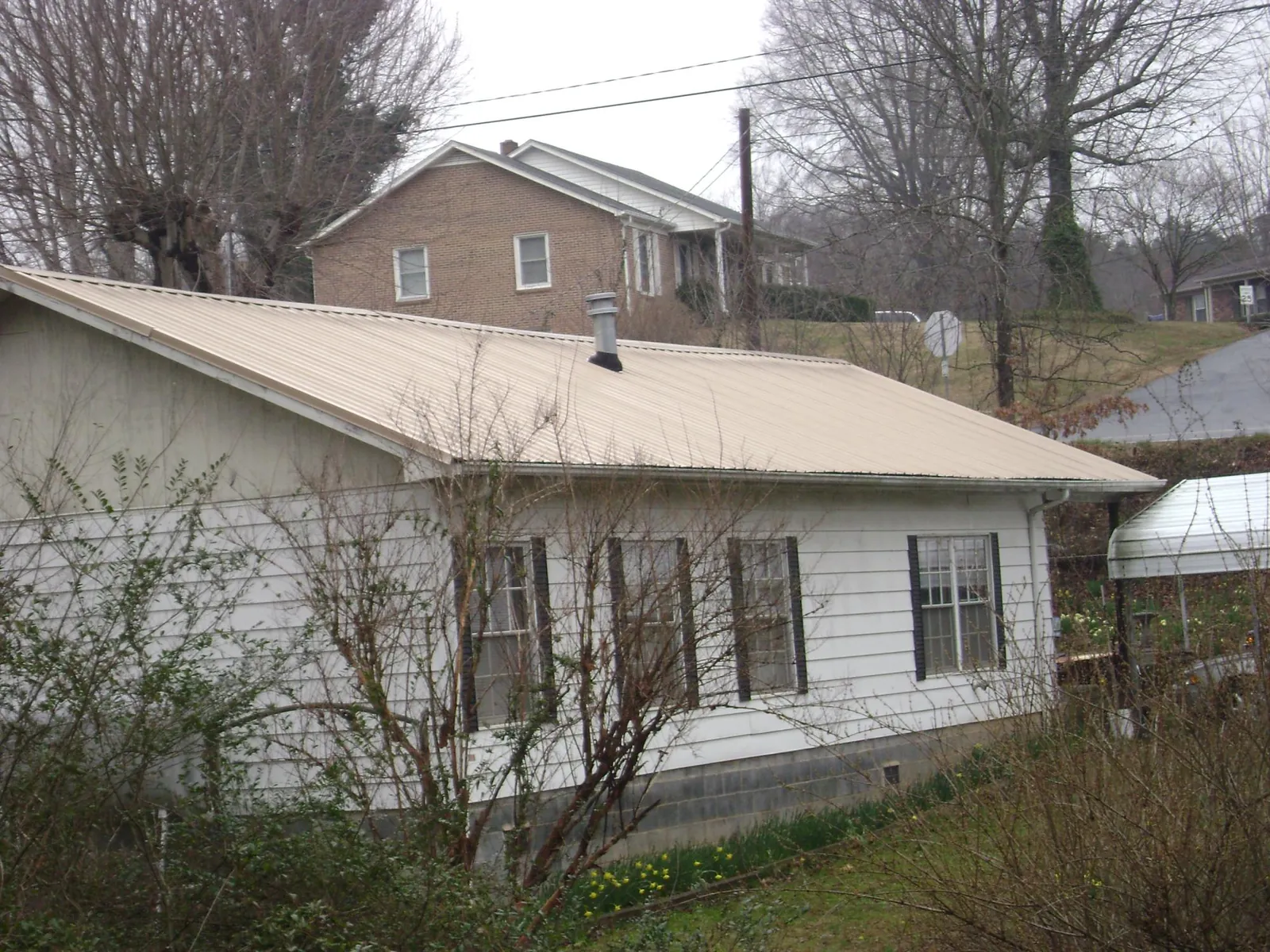Tan metal roof on a white sided house set into a hillside — Commercial Roofing by Roofing Brothers in Fort Gratiot