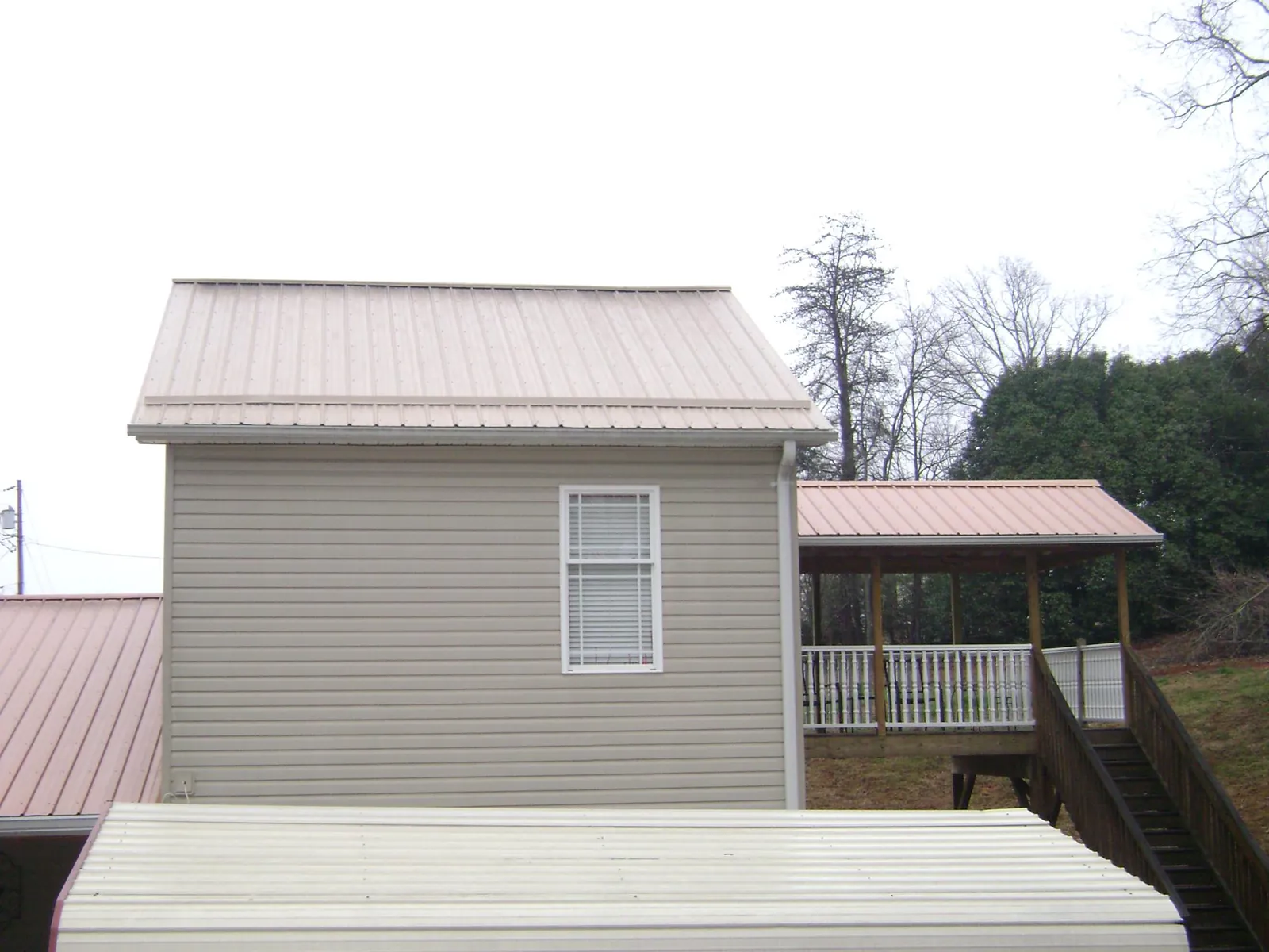 Tan metal roofs on a two story addition and attached porch, from a Roof Replacement job in Fort Gratiot