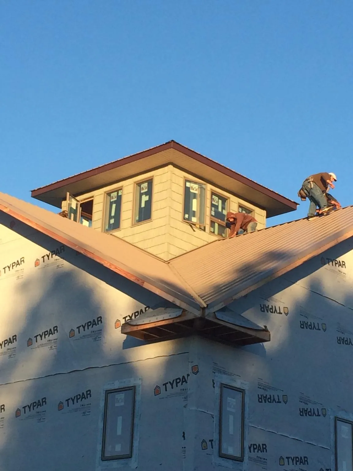 Roofers working around a rooftop cupola on a new metal roof at sunset — Roof Waterproofing in Fort Gratiot by Roofing Brothers